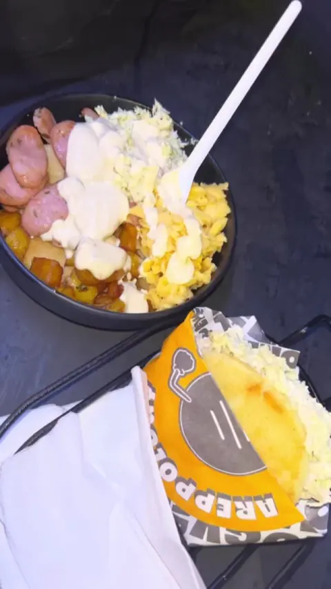 Bowl con salchicha, papa y queso, junto a una arepa