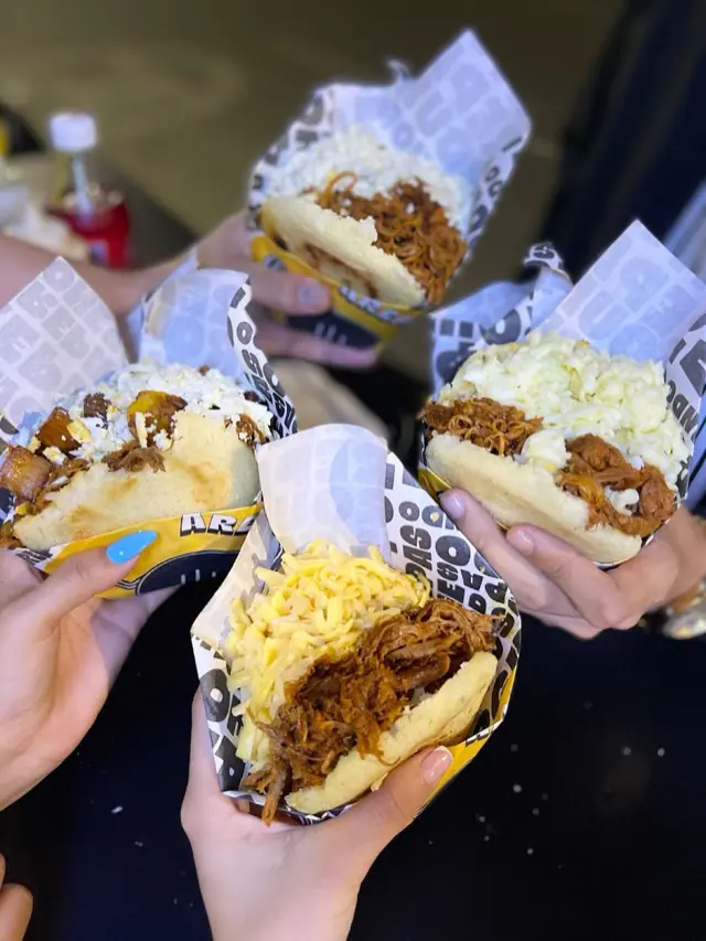 Cuatro arepas rellenas en la mano, con carne desmechada y queso